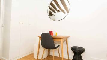 A room with a wooden desk, a black chair, a round mirror, and a small black stool.