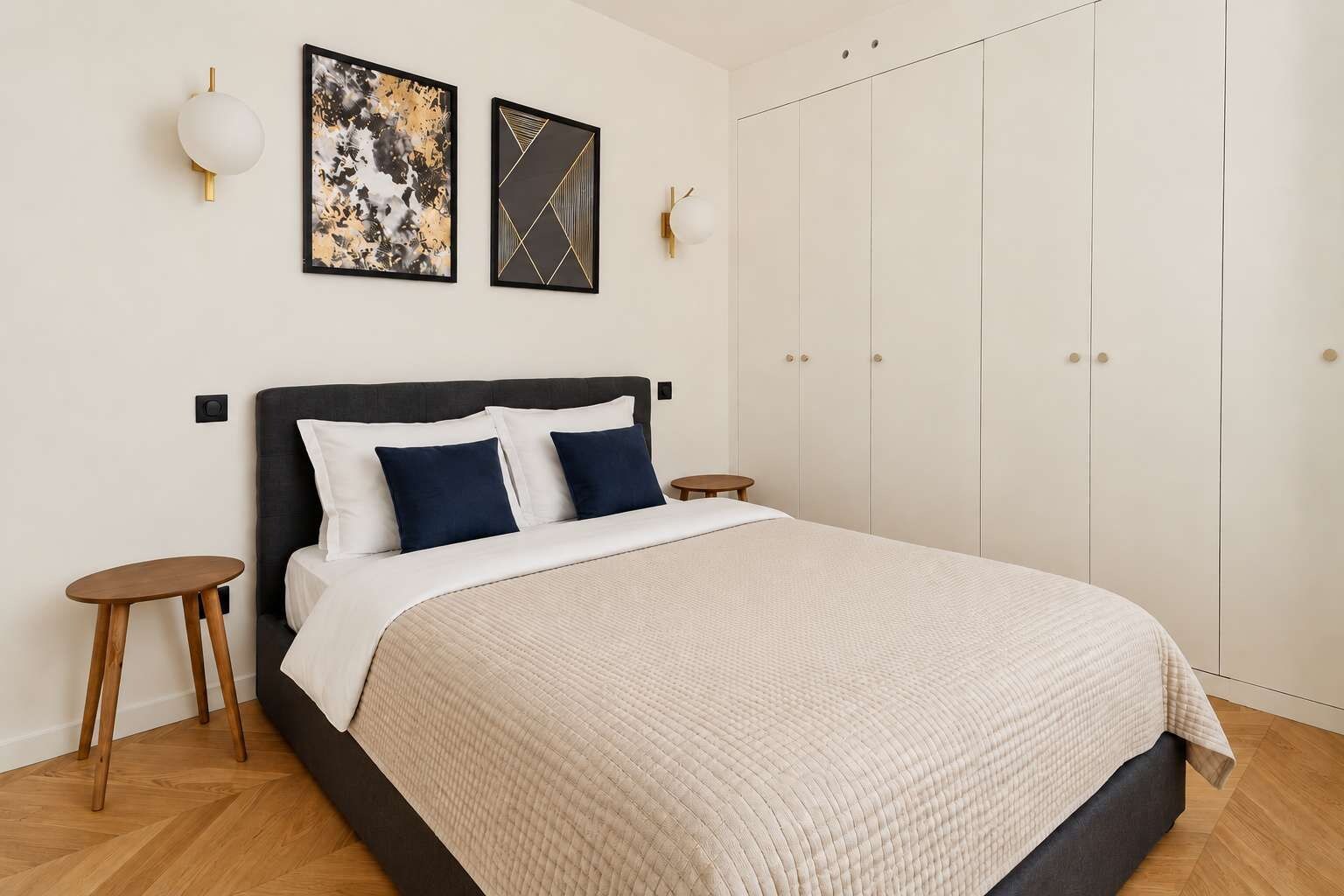 A bedroom with a bed, two bedside tables, a wardrobe, and two wall-mounted light fixtures.
