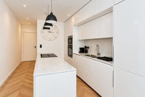 Une cuisine moderne avec des meubles blancs, un plan de travail en marbre et un luminaire suspendu noir.