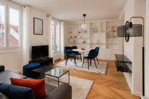 Een moderne woonkamer met een televisie, een bank en een eethoek met stoelen.