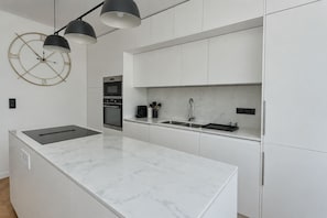 A modern kitchen with a marble countertop, built-in oven, and a clock on the wall. - Lovely 2-Bedroom by Saint Lazare - Madeleine (Paris)