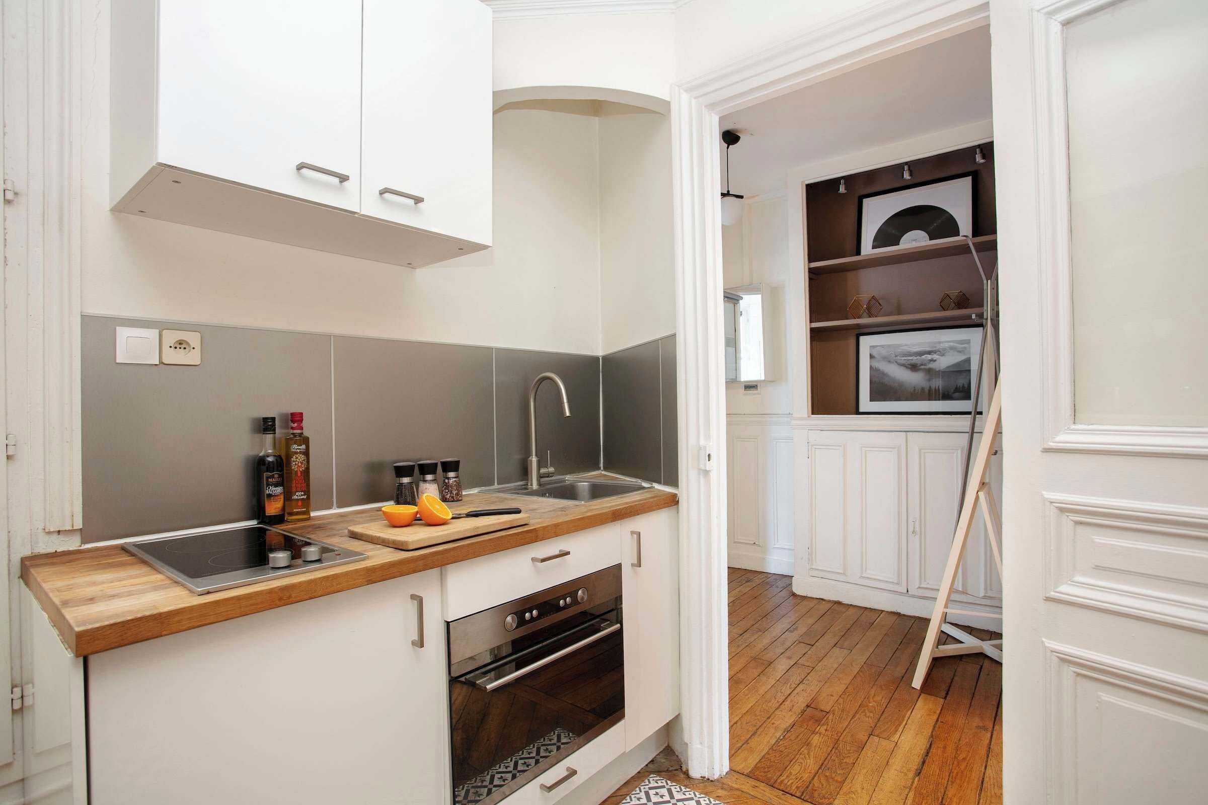 Une cuisine compacte avec des meubles blancs, un plan de travail en bois, un four encastré et un évier.