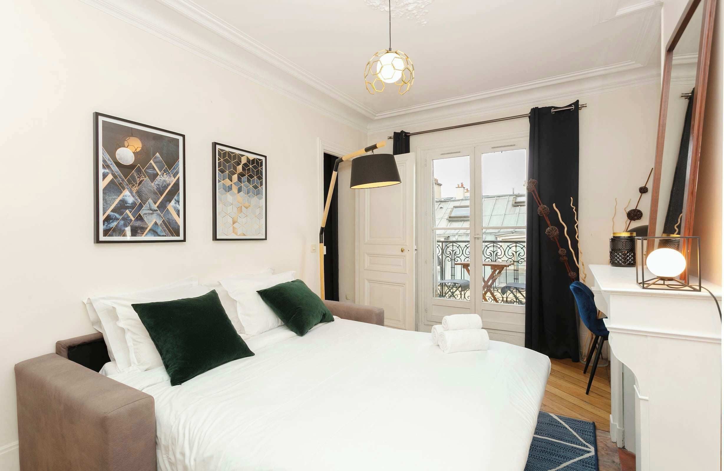 Une chambre d’hôtel comprenant un lit, un bureau, une chaise, un balcon avec vue et deux œuvres d’art encadrées accrochées au mur.
