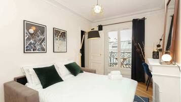 Une chambre d’hôtel comprenant un lit, un bureau, une chaise, un balcon avec vue et deux œuvres d’art encadrées accrochées au mur.