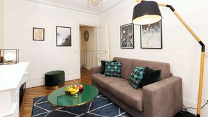 Un salon avec une table basse verte, un canapé marron agrémenté de coussins à motifs, un lampadaire et des tableaux encadrés accrochés au mur.