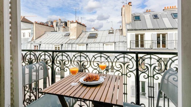Un balcon avec une table préparée pour le petit-déjeuner, comprenant des croissants et du jus d’orange.