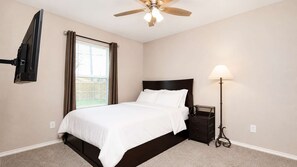 A bedroom with a bed, a ceiling fan, a nightstand, a lamp, and a TV mounted on the wall.