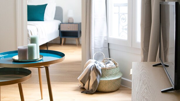 Ein Hotelzimmer mit Bett, Fernseher, Tisch mit Kerzen, Korb und einem Fenster mit Vorhängen.