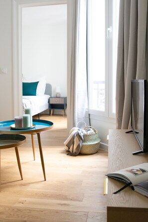 A hotel room with a bed, a TV, a table with candles, a basket, and a window with curtains. - Charming 1BR in the Heart of Montorgueil Area (Paris)
