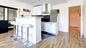 A modern kitchen with a central island, bar stools, and a sign listing Paris landmarks. - Lovely 1BR Flat by Palais Royal-Le Louvre (Paris)