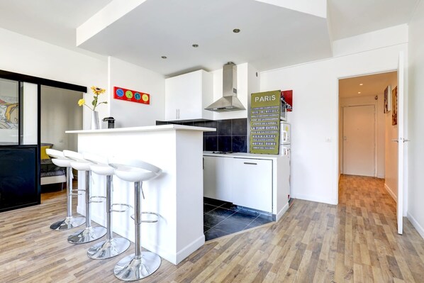 A modern kitchen with a central island, bar stools, and a sign listing Paris landmarks.