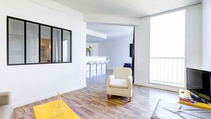 A modern living room with a large window, a TV, and a yellow table with a model of the Eiffel Tower. - Lovely 1BR Flat by Palais Royal-Le Louvre (Paris)