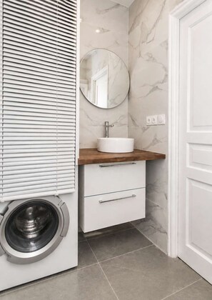 Un baño pequeño con lavadora integrada, un lavamanos con encimera de madera y un espejo.