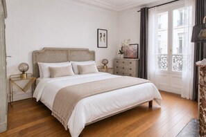 Un dormitorio con cama, mesitas de noche, cómoda y ventana con cortinas.