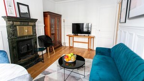 Un salon avec une cheminée, un téléviseur, un canapé bleu et une table basse sur laquelle se trouvent des fruits.