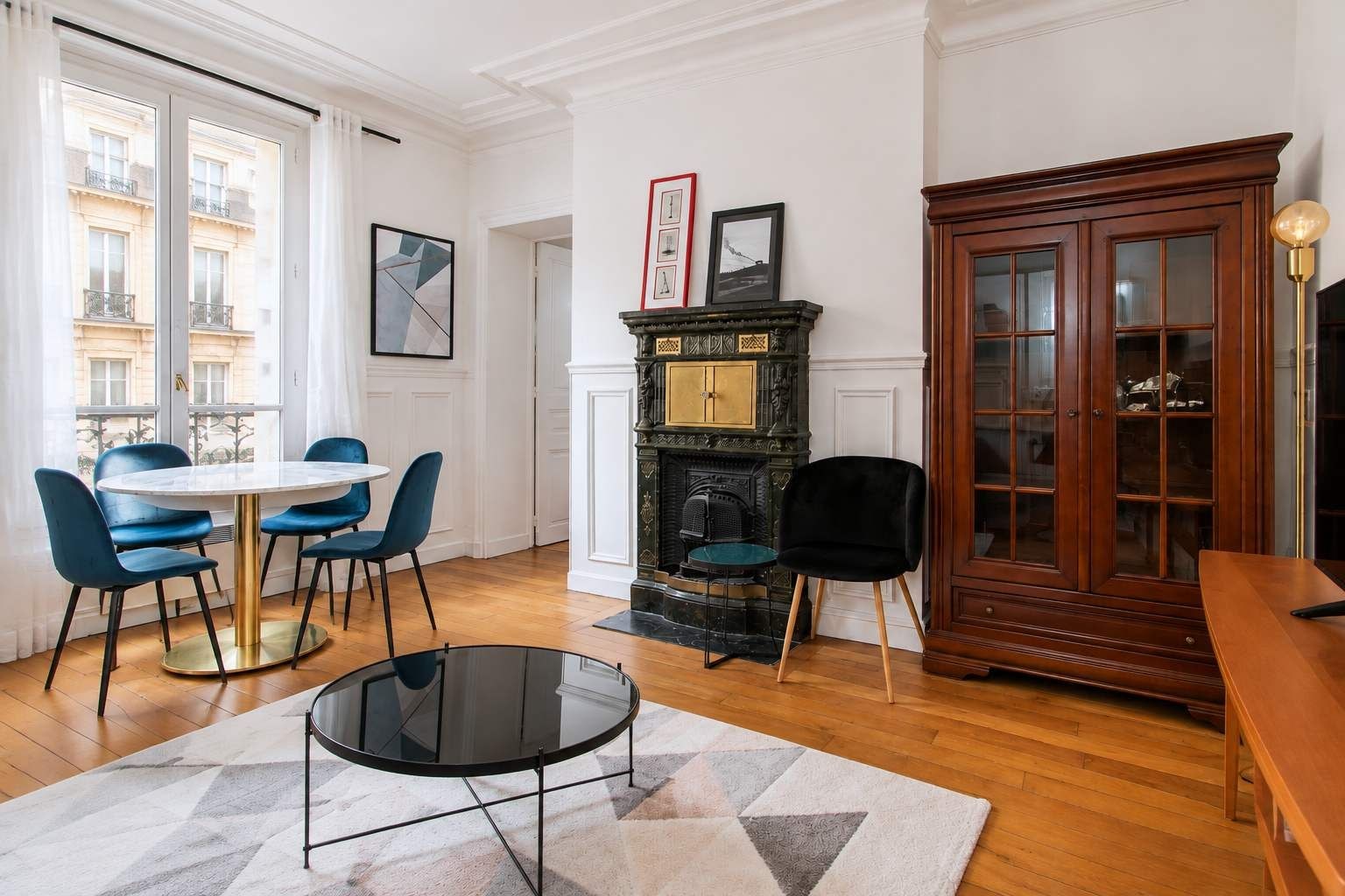 A room with a round table, blue chairs, a fireplace, and a wooden cabinet.