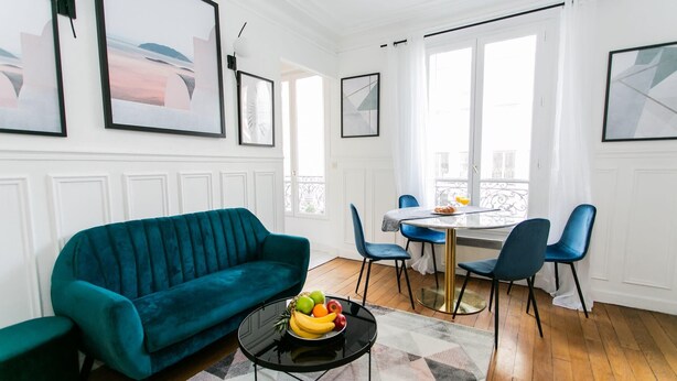Un salon avec un canapé de couleur turquoise, une table à manger avec des chaises et un panier de fruits posé sur une table basse.