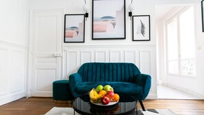 Un canapé de couleur turquoise, une table ronde noire sur laquelle sont disposés des fruits, et des œuvres d’art encadrées accrochées au mur.