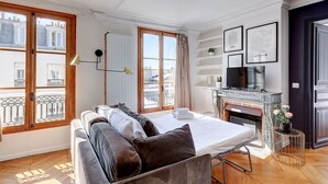 Un dormitorio moderno con cama, sofá, chimenea y ventanas amplias con vista a la ciudad.