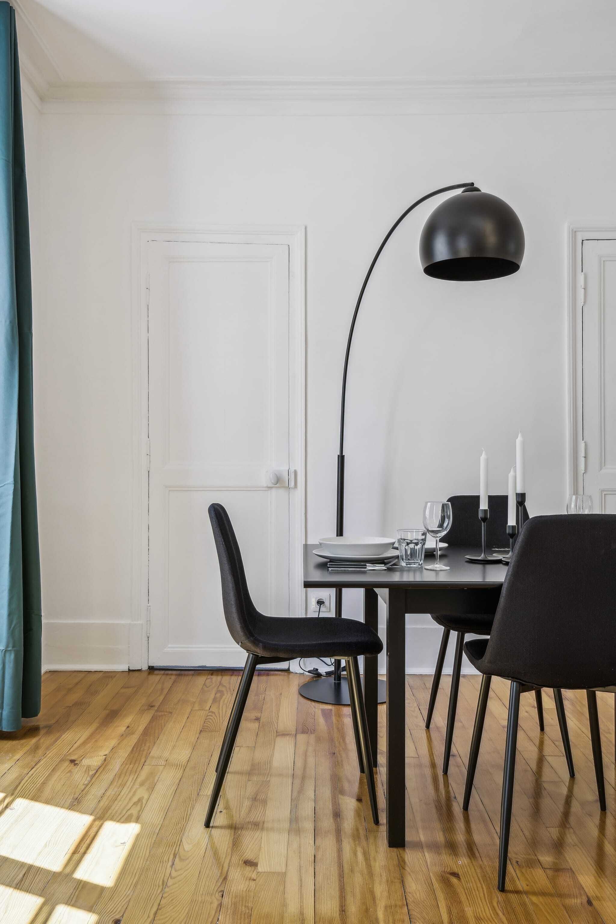 A dining area with a wooden table, black chairs, a black floor lamp, and white candles.