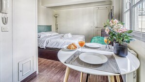 A hotel room with a dining table set for breakfast, a bed with a striped bedspread, and a window with a view. - Cozy Studio in The Heart of Latin Quarter (Paris)