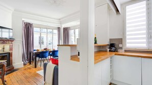 A modern kitchen with white cabinets, a wooden countertop, and a dining area with a table and chairs. - Stylish 2BR Steps from Louvre - Place Vendome (Paris)