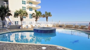 A swimming pool with lounge chairs and palm trees, surrounded by a building with balconies. - Beachfront-Pool-Balcony-Wonderful View (Gulf Shores)