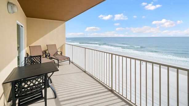 A balcony with a view of the ocean, a table, two chairs, and a railing. - Beachfront-Pool-Balcony-Wonderful View (Gulf Shores)