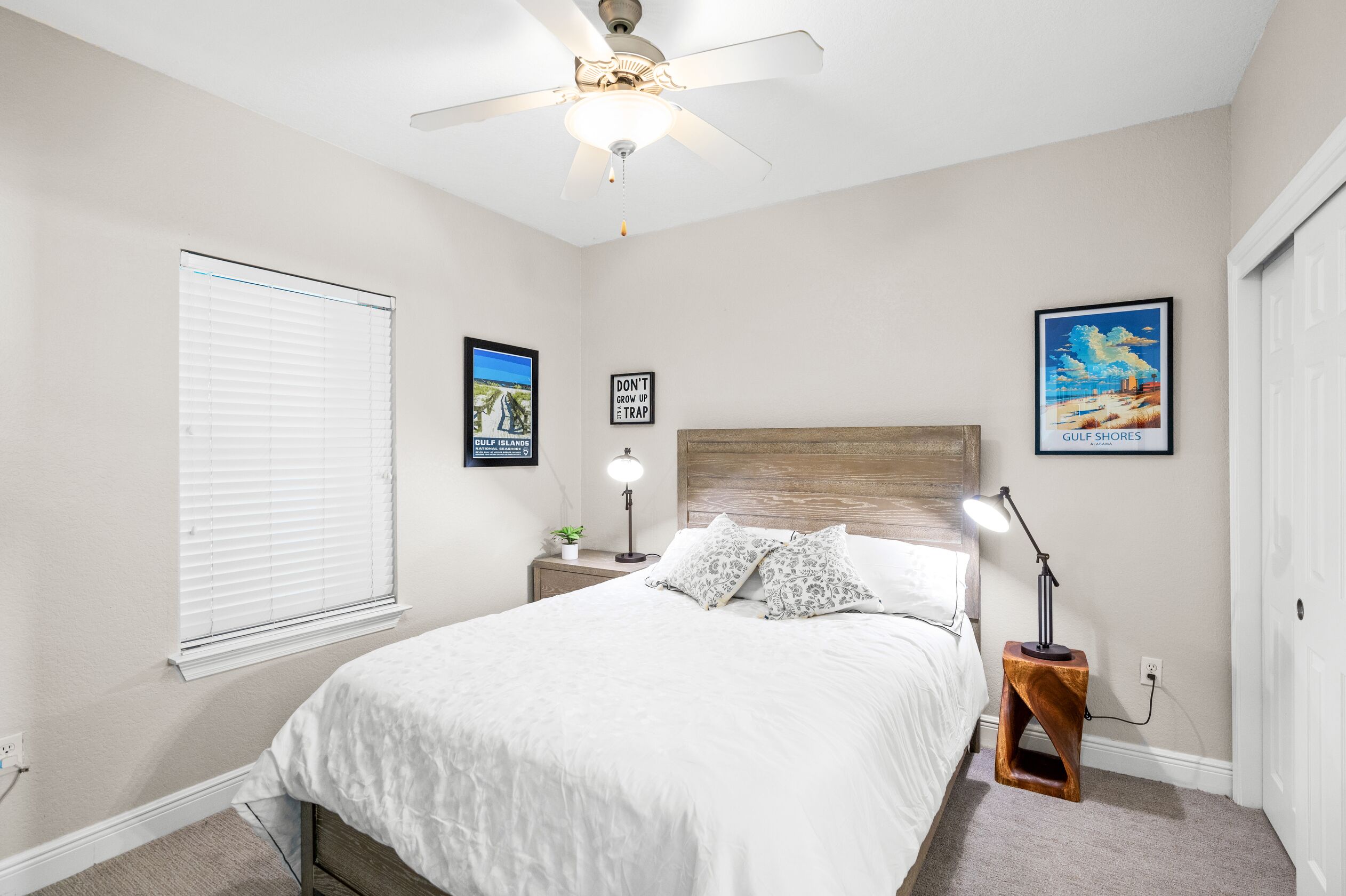 A bedroom with a bed, bedside table, lamp, ceiling fan, and wall art.