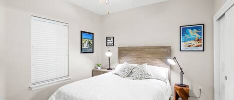 A bedroom with a bed, bedside table, lamp, ceiling fan, and wall art.