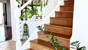 A wooden staircase with white railings, surrounded by green plants and a birdcage.