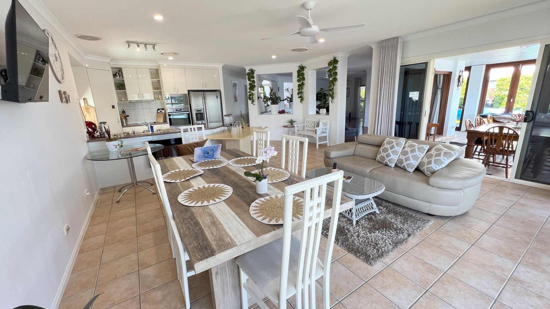 A modern kitchen with white cabinets, a dining area with a wooden table and white chairs, and a living room with a beige sofa and a coffee table.