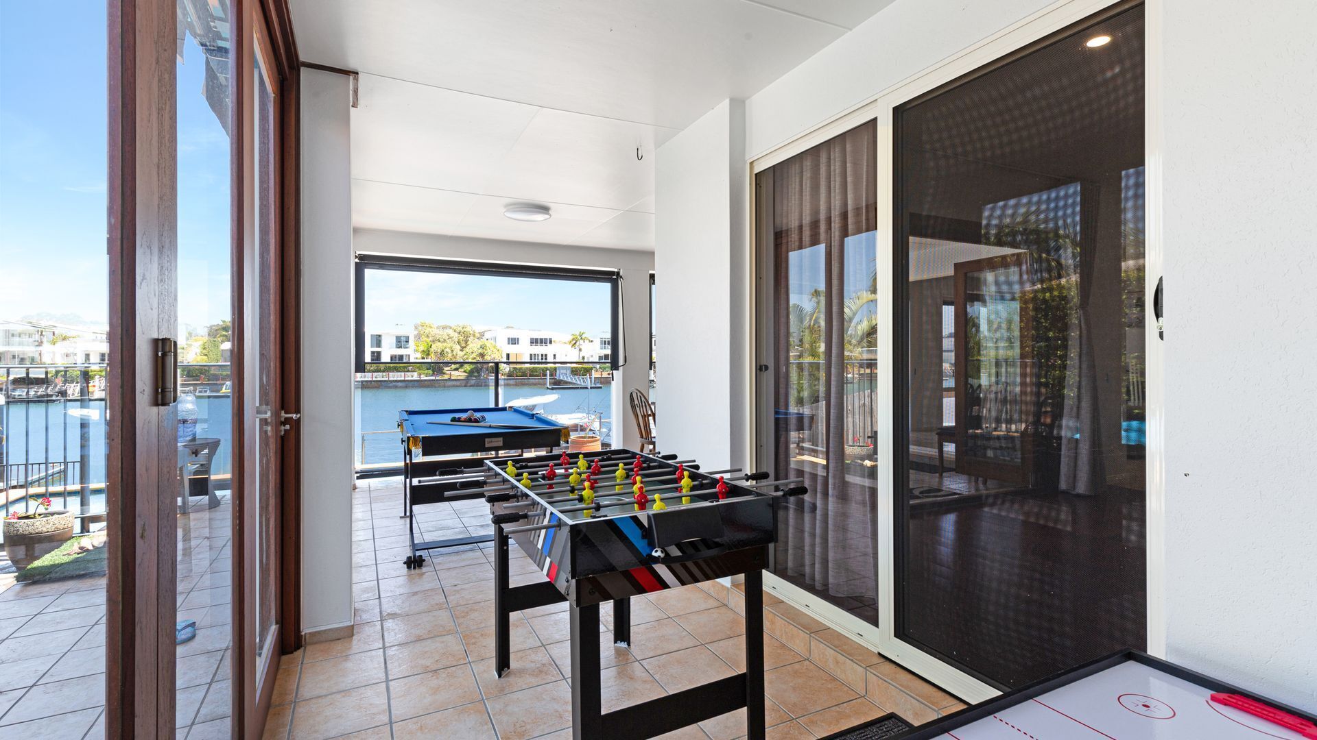 Habitación con mesa de fútbol, puerta corrediza a un balcón y vista a un puerto deportivo.