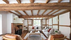 Ein rustikales Wohnzimmer mit sichtbaren Holzbalken, einem Kamin aus Ziegelsteinen und einer gemütlichen Sitzecke mit Ledersesseln und einem Sofa.