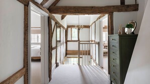 Ein schmaler Flur mit freiliegenden Holzbalken, einer weißen Tür zu einem Schlafzimmer und einer grünen Kommode mit Schubladen.