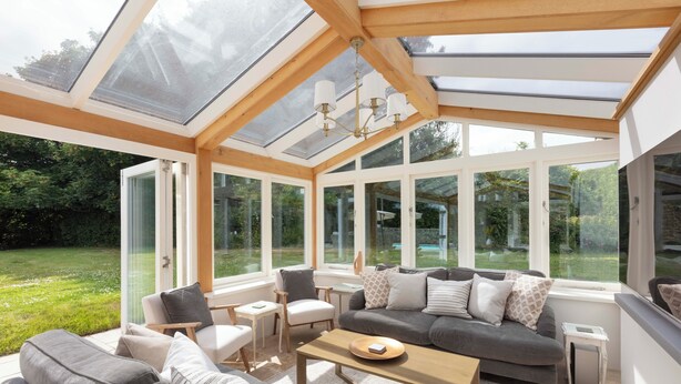 Ein Wintergarten mit modernem Interieur, großen Fenstern und einer Holzbalkendecke.