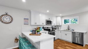 A modern kitchen with white cabinets, stainless steel appliances, and a central island. - Hidden Renovated Garden Cottage Near Costco, I99 (Shoreline)