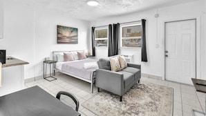 Habitación de hotel compacta con cama, sofá, mesa de comedor y pequeña cocina.