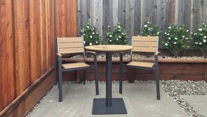A wooden deck with a round table and two chairs, surrounded by a wooden fence and plants.