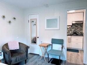 Une pièce de taille modeste comprenant un canapé, une petite table, une chaise, un miroir et un coin cuisine.