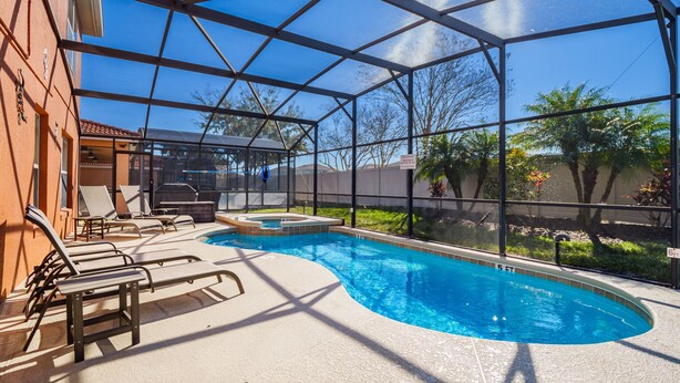 A swimming pool with lounge chairs and a hot tub, surrounded by a covered area with a view of trees and a building. - ⭐⭐5 Bed, 4 Bath Property | SOUTH Facing Pool | Gated Resort | Mins to Disney ⭐⭐ (Davenport)