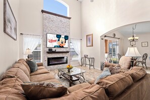 A living room with a fireplace, a large flat-screen TV, a sofa, and a coffee table with fruit.