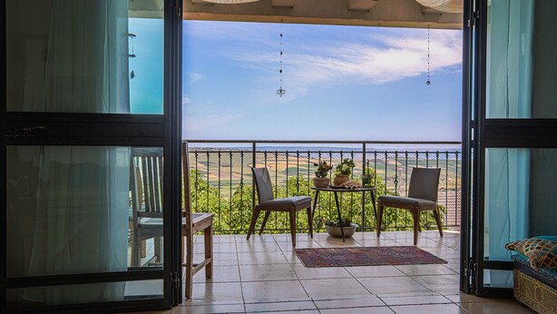 An open balcony with a view of a green landscape, two chairs, a small table with potted plants, and a hanging light fixture. - Loveneel Sea Galilee Retreat by SeaNRent (Yavne'el)