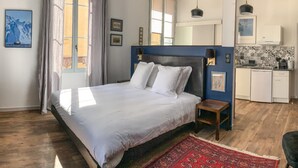 Un dormitorio con una cama grande, piso de madera, alfombra roja, una mesita, un escritorio, una kitchenette y un baño.