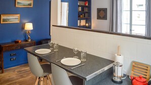 Un comedor con una mesa preparada para dos personas, sillas, una lámpara y una estantería al fondo.