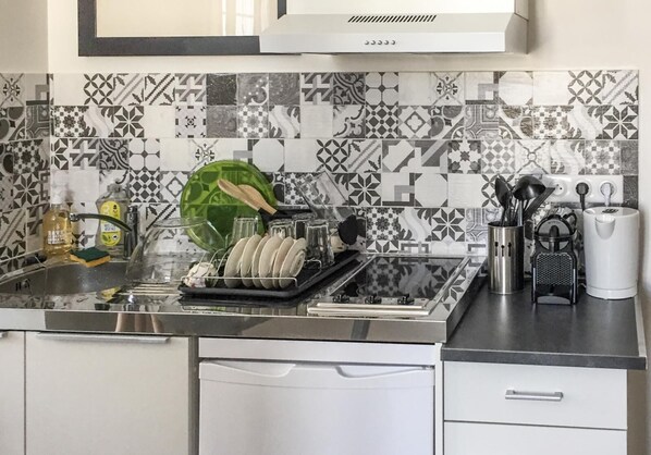A kitchen with a patterned backsplash, a dish rack with plates, a coffee maker, and a kettle.