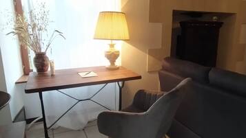 Un petit salon moderne, avec un canapé gris foncé, une table en bois surmontée d’une lampe et une plante en pot.