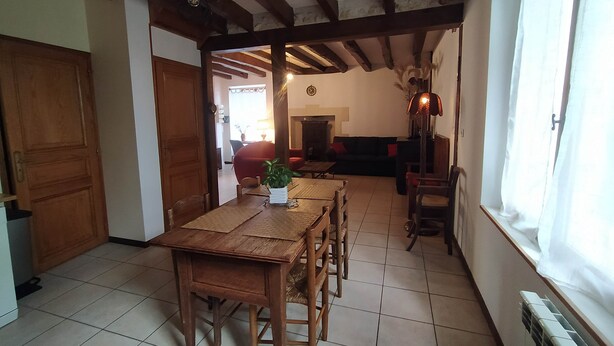 A dining area with a wooden table and chairs, a potted plant, and a view of a living room with a sofa and a fireplace. - Maison de Caractère, Jardin Clos , au Calme, Proche zoo de Beauval et Châteaux (Écueillé)