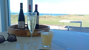 Una mesa con una botella de vino, una copa de vino blanco, un vaso con una bebida amarilla y carne en una tabla de cortar.