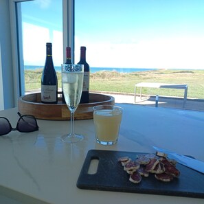 A table with a bottle of wine, a glass of white wine, a shot glass with a yellow drink, and sliced meat on a cutting board. - Nouveau Villa " Côte et Mer" Cap Gris Nez Animaux de Compagnie Acceptés (Audinghen)